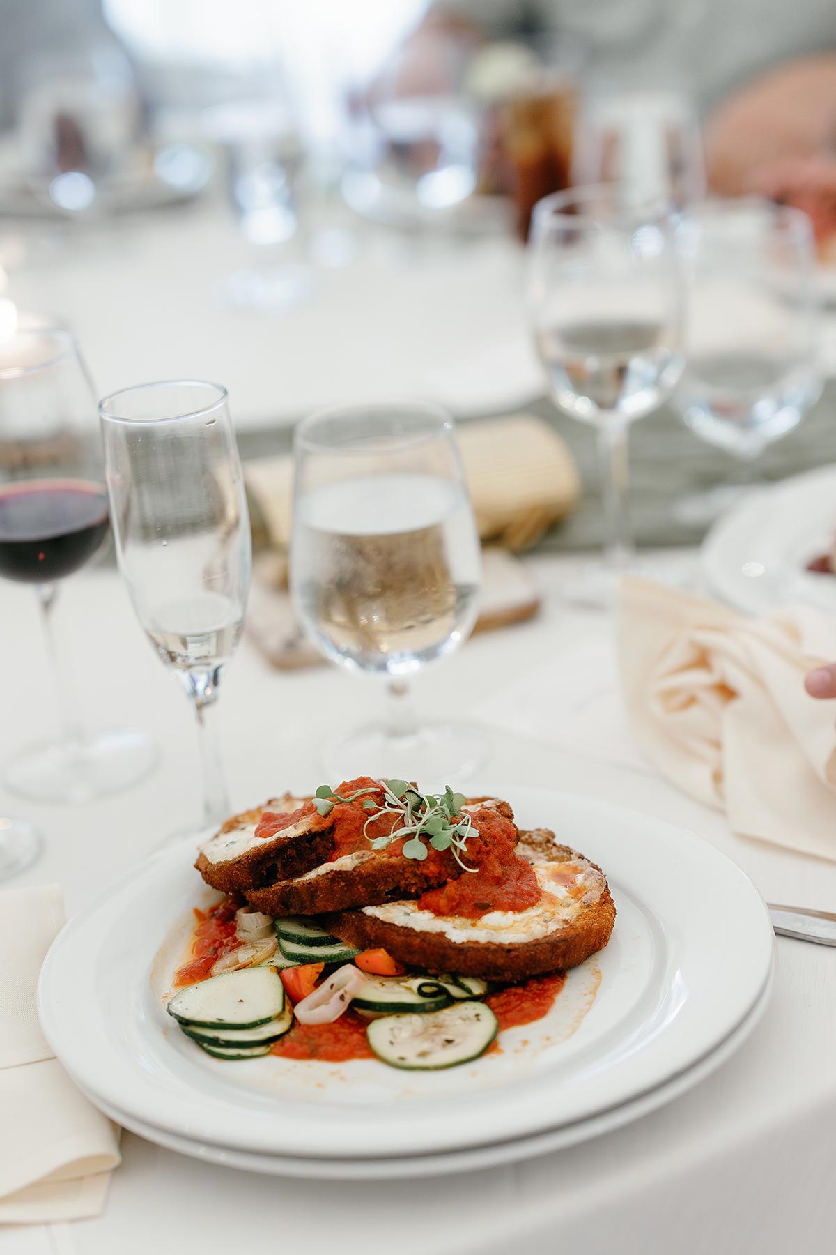 Plate of stuffed pasta in tomato sauce with zucchini, surrounded by wine glasses.