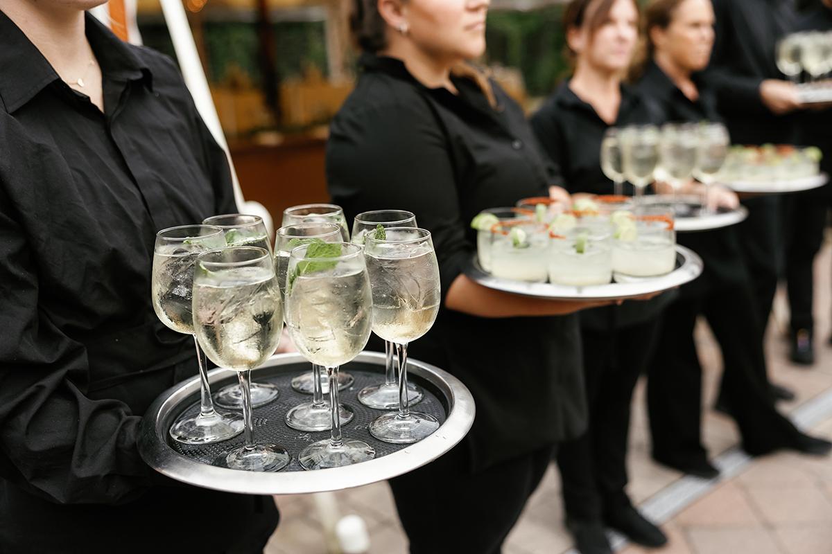 Servers in black uniforms holding trays of cocktails.