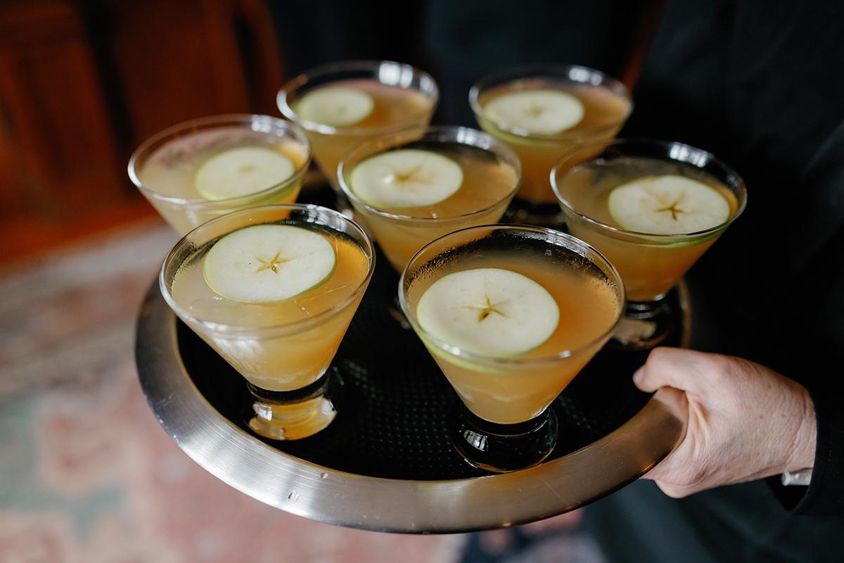 Seven cocktails with apple slices on a tray.