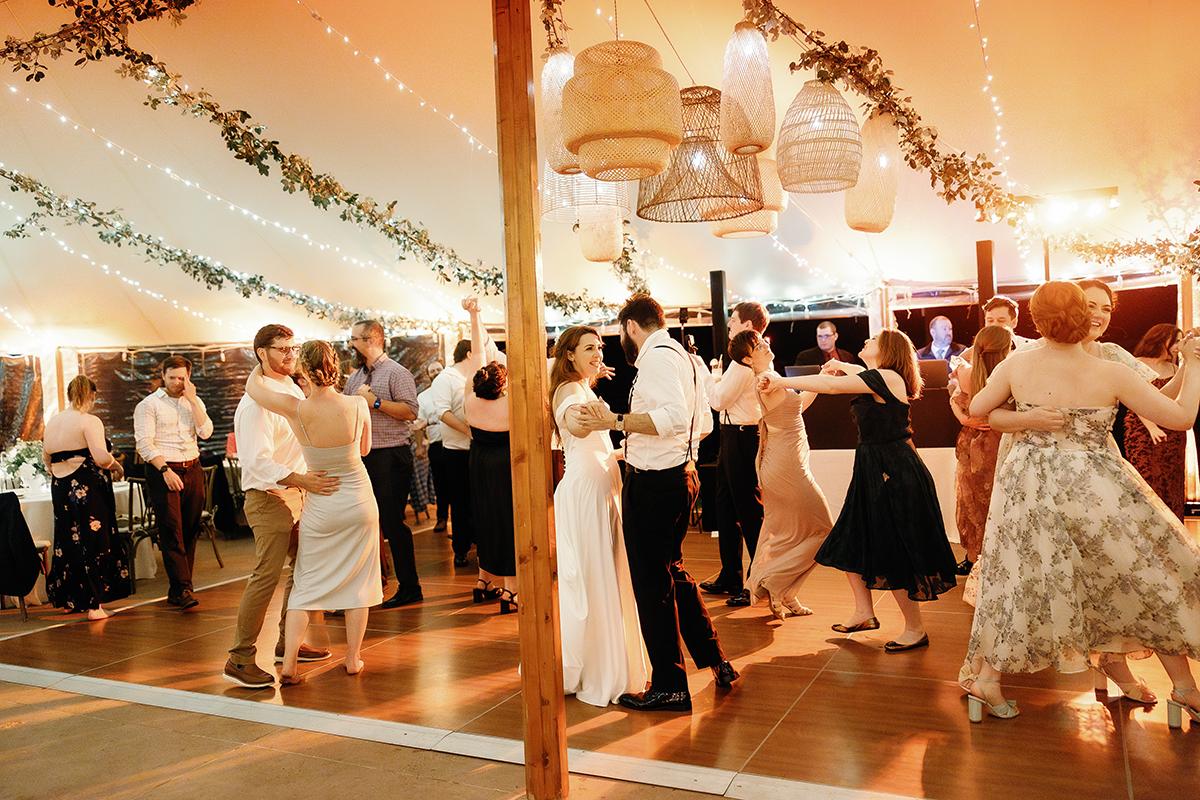 Dancing couples under string lights at a lively indoor wedding reception.