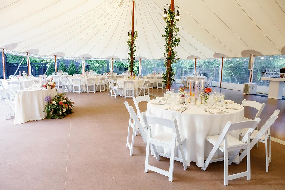 Wedding tent with round tables, white chairs, and floral centerpieces.