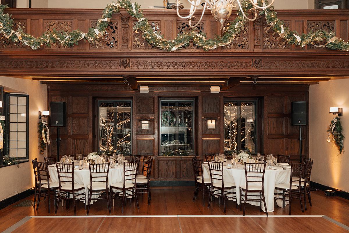 Elegant banquet hall with decorated tables, chandeliers, and garland.