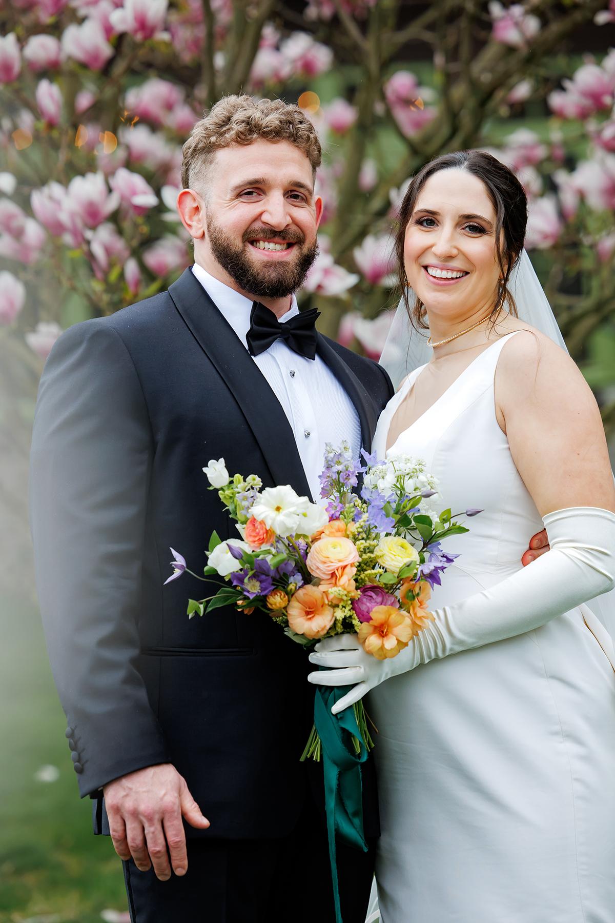 Bride and groom smiling in front of blooming magnolia tree.