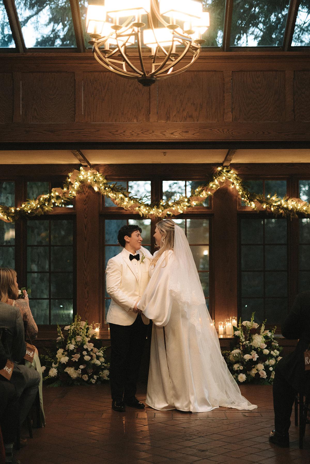 Couple exchanging vows in a warmly lit room decorated with garlands.