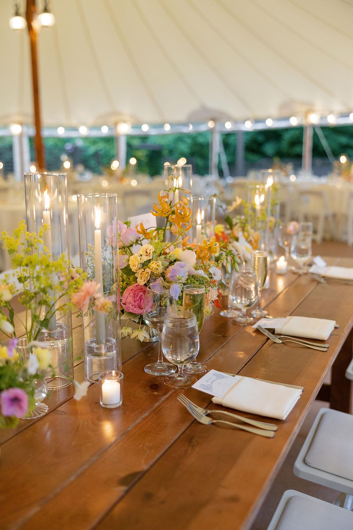 Elegant wedding table with floral centerpieces and candles under a tent.