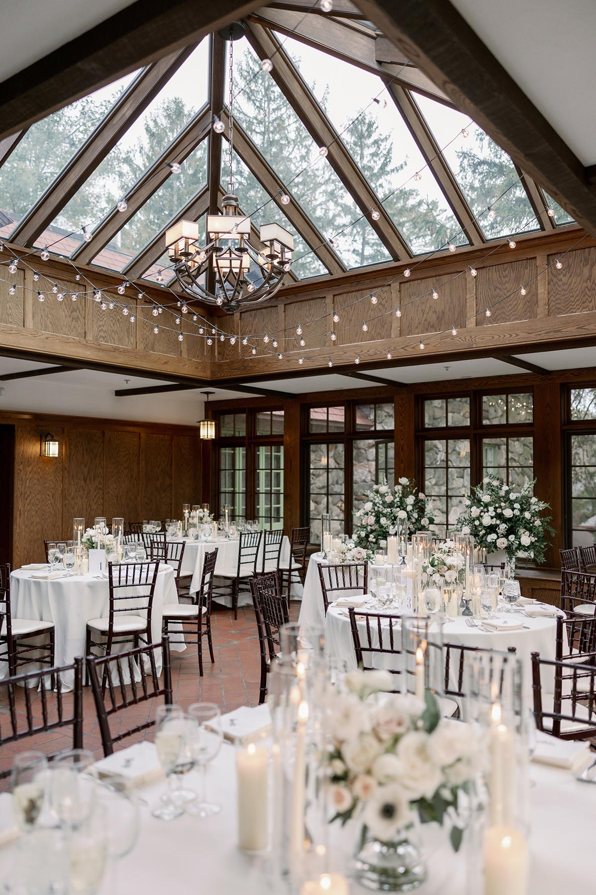 Elegant dining hall with skylights, white flowers, and candlelit tables.