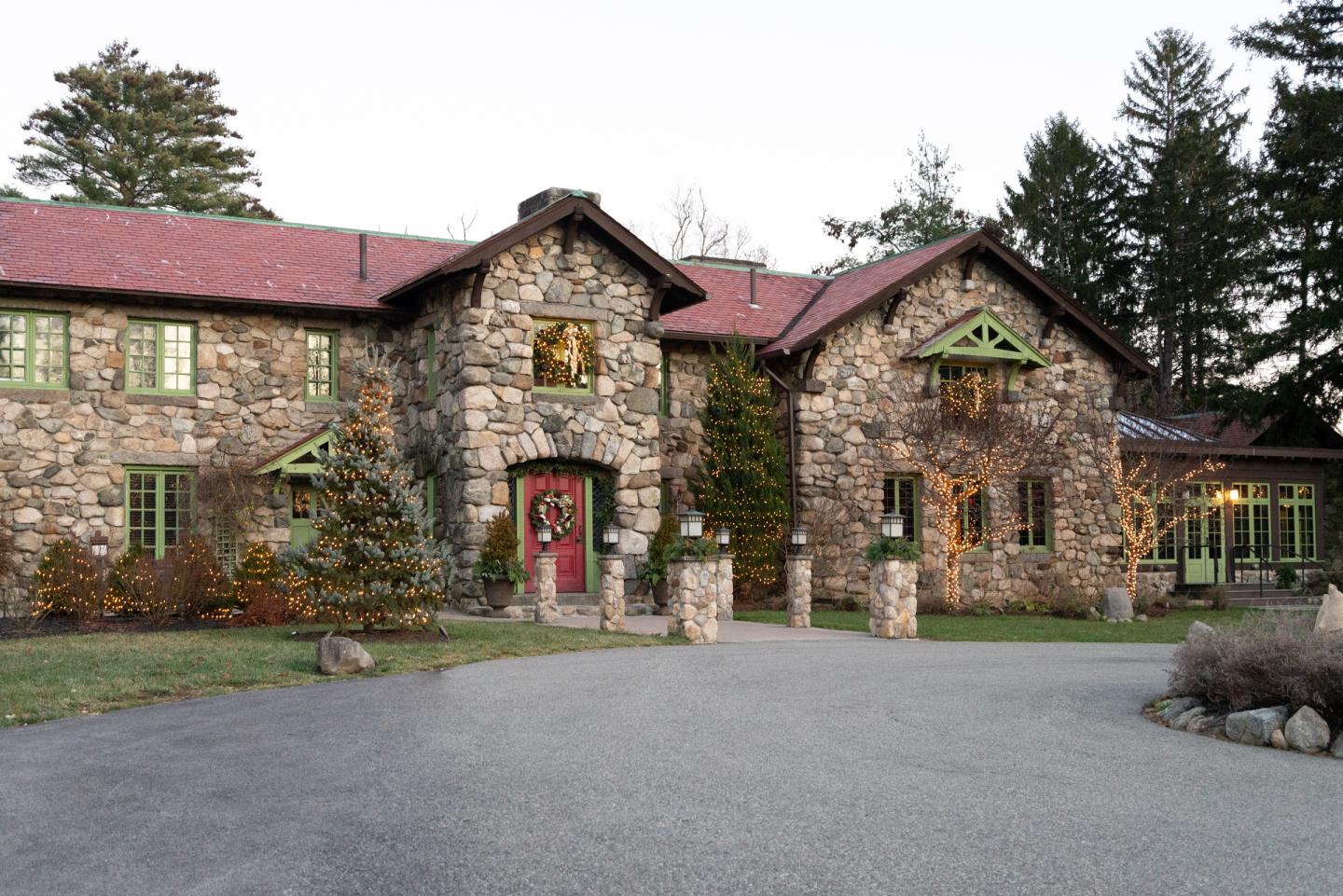 Stone house with red roof, surrounded by trees, adorned with festive wreaths.