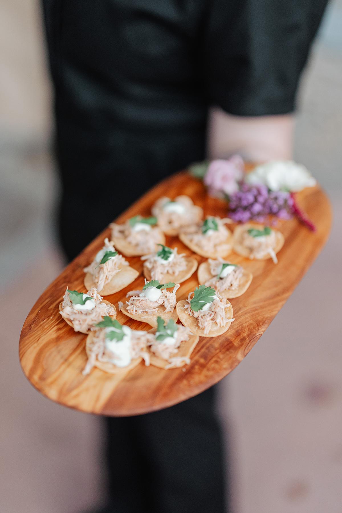 Appetizers on a wooden platter garnished with herbs and flowers.