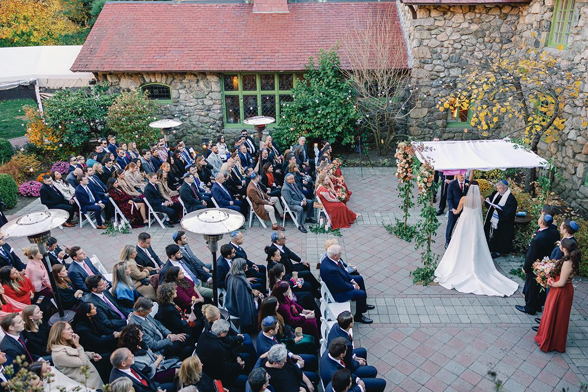 Wedding ceremony outdoors, bride and groom under canopy, guests seated nearby.