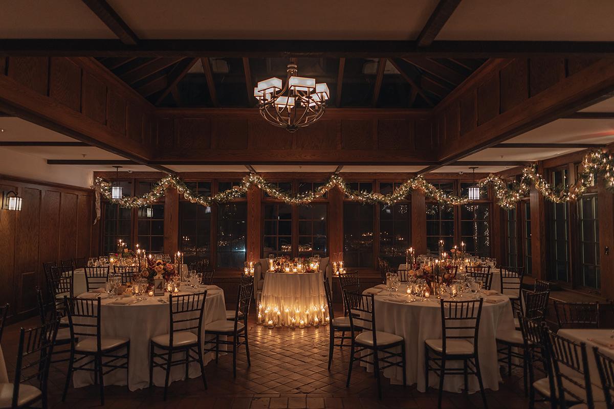 Elegant dining hall with round tables, candles, and string lights.
