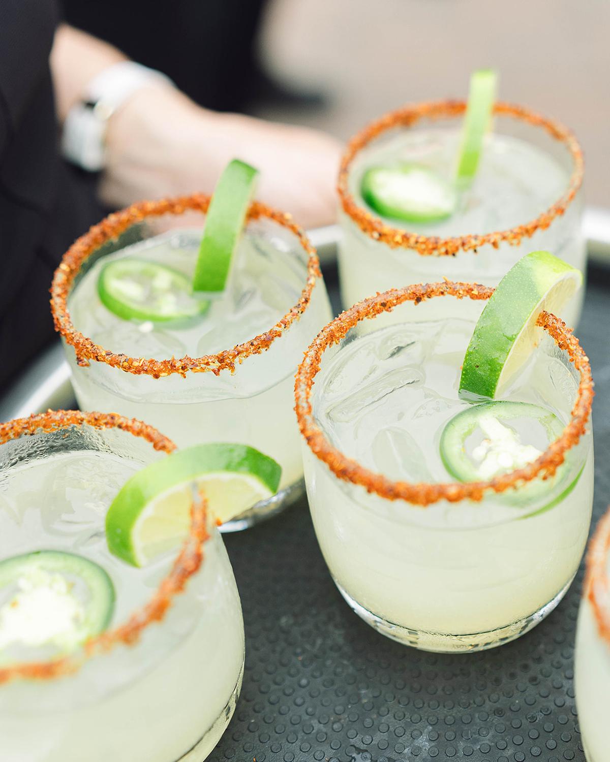 Four margaritas with lime slices and jalapeños, rimmed with chili salt.