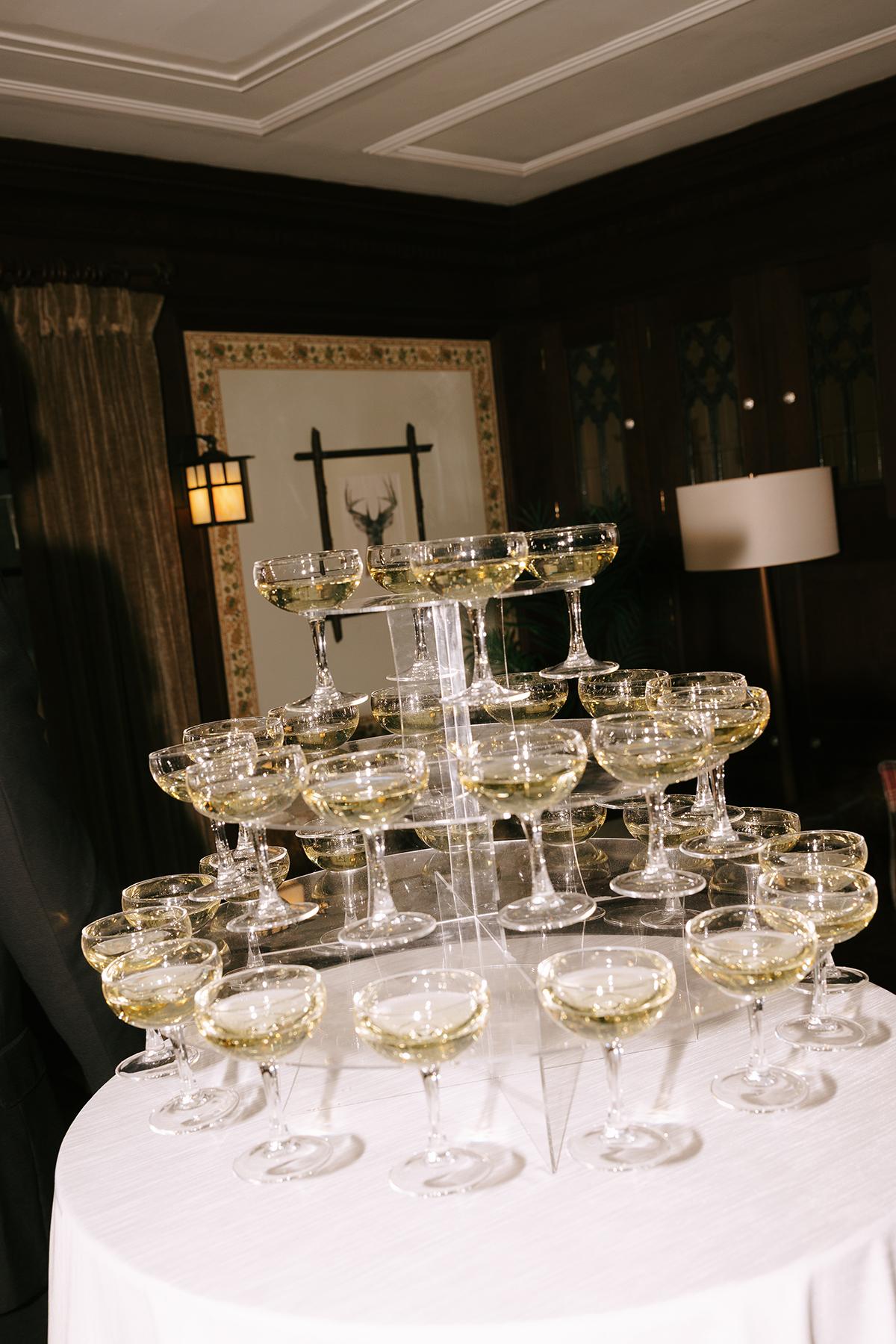 Champagne glasses stacked in a pyramid on a round table indoors.