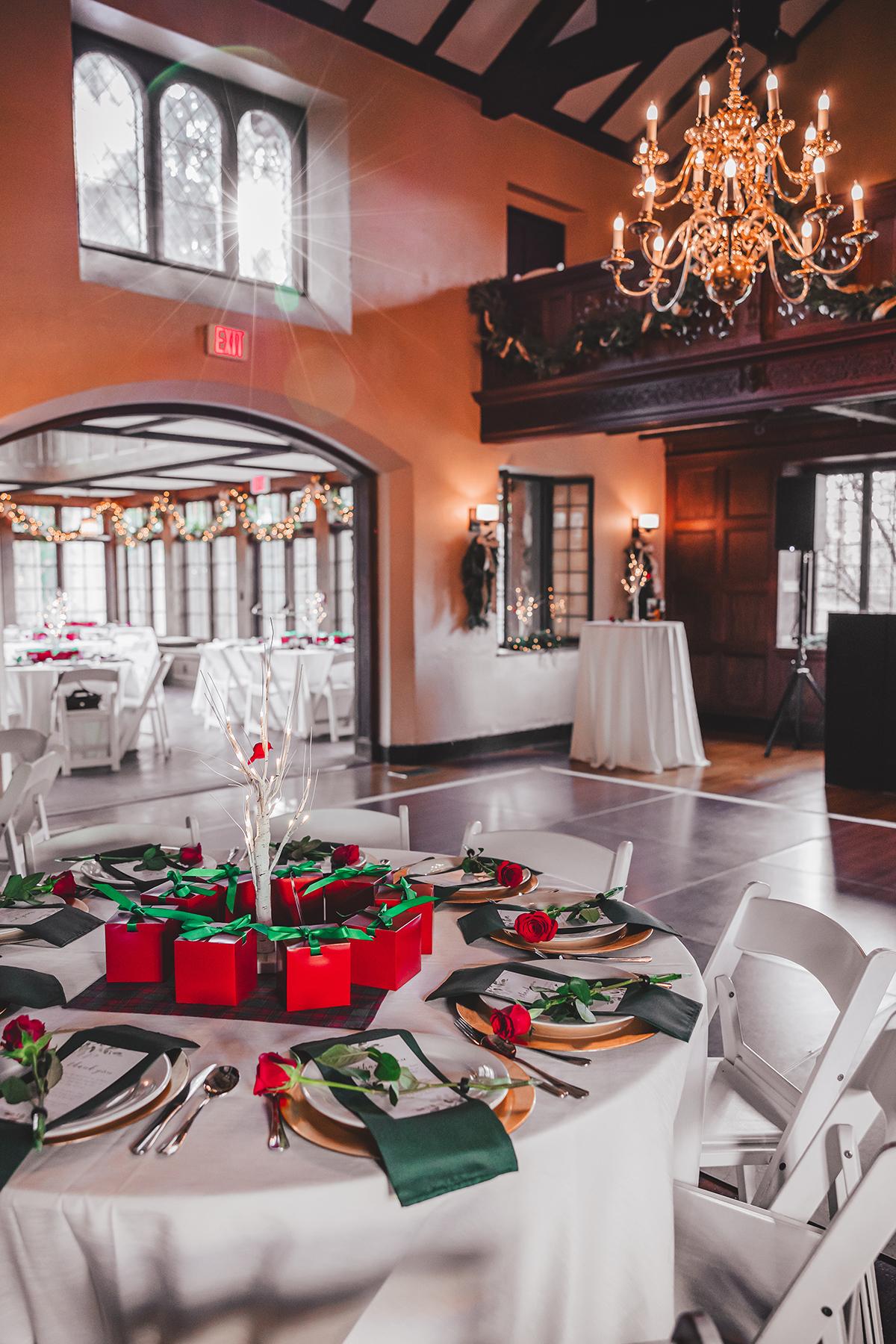 Elegant dining room with decorated tables, red gift boxes, and a chandelier.