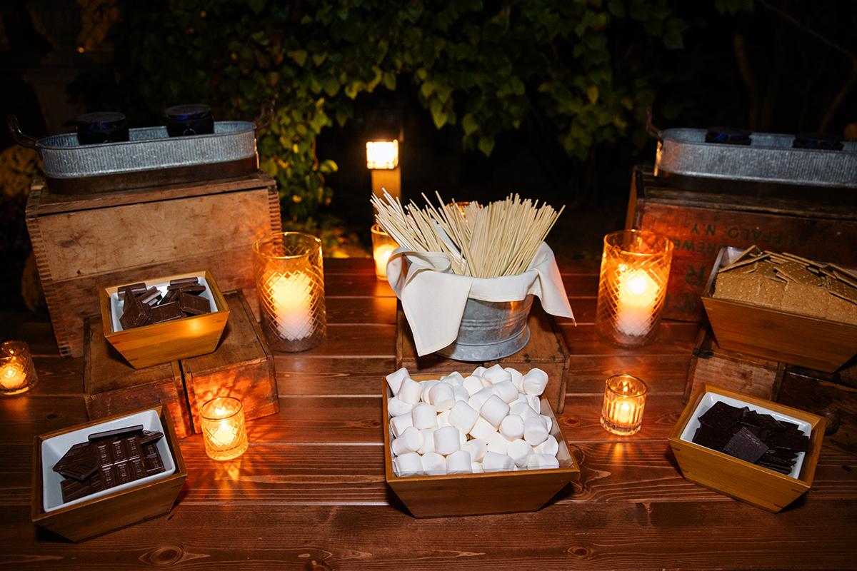 S'mores station with marshmallows, chocolate, and candles on a wooden table.