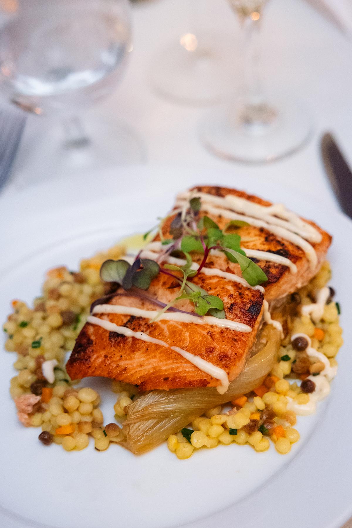 Grilled salmon on couscous with herbs, drizzled with sauce.
