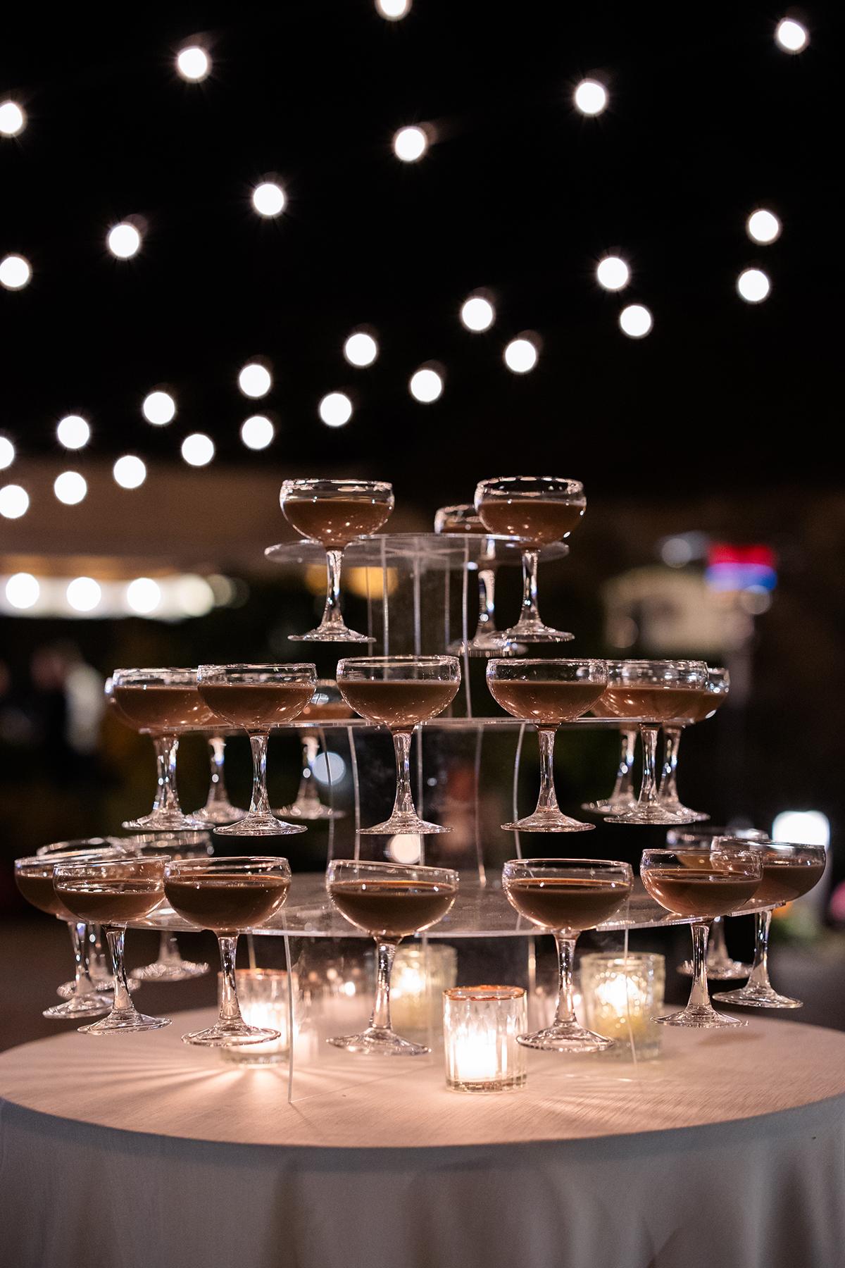 espresso martini tower with candles on a table, under string lights at night.