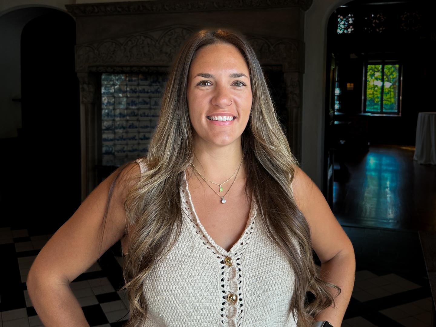 Smiling woman with long hair stands in a dimly lit room.