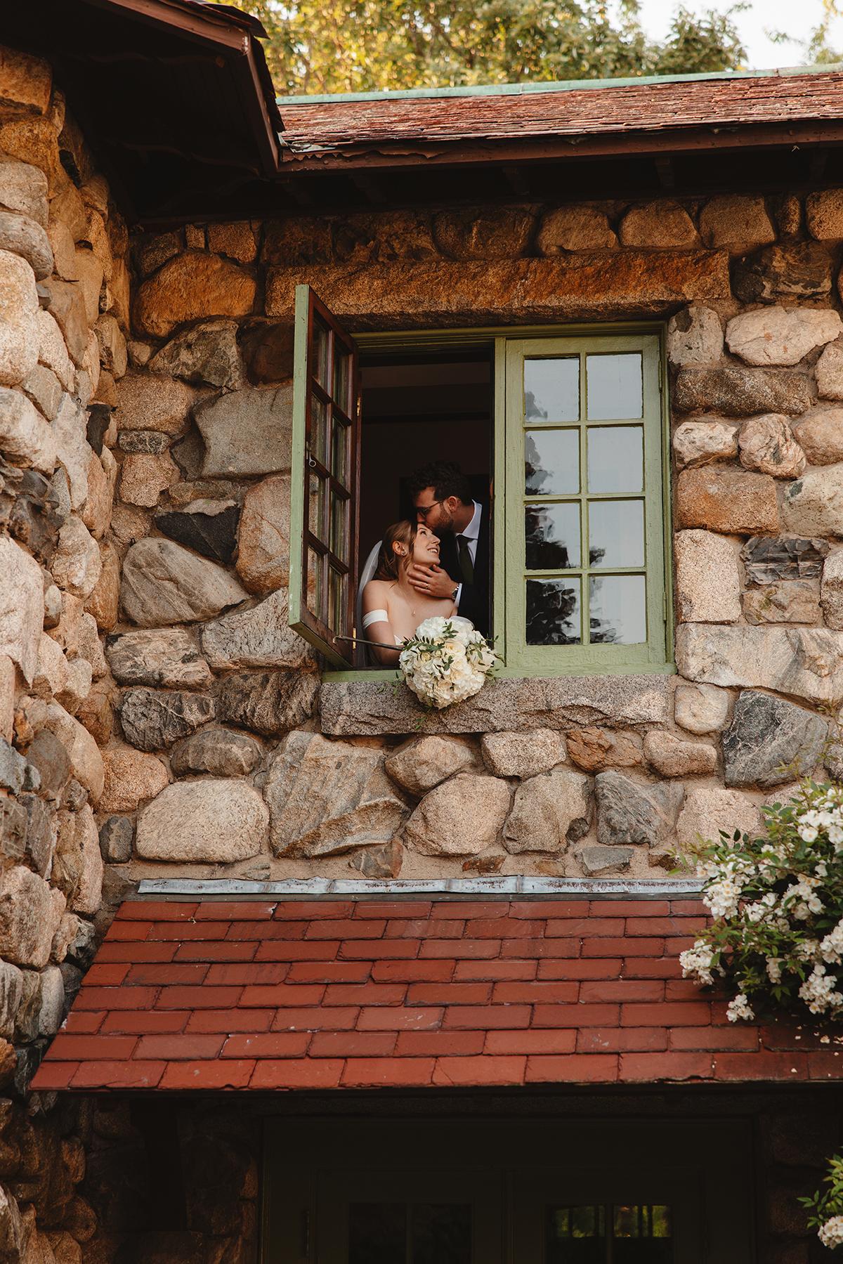 Couple kissing in a stone building window, bouquet nearby.