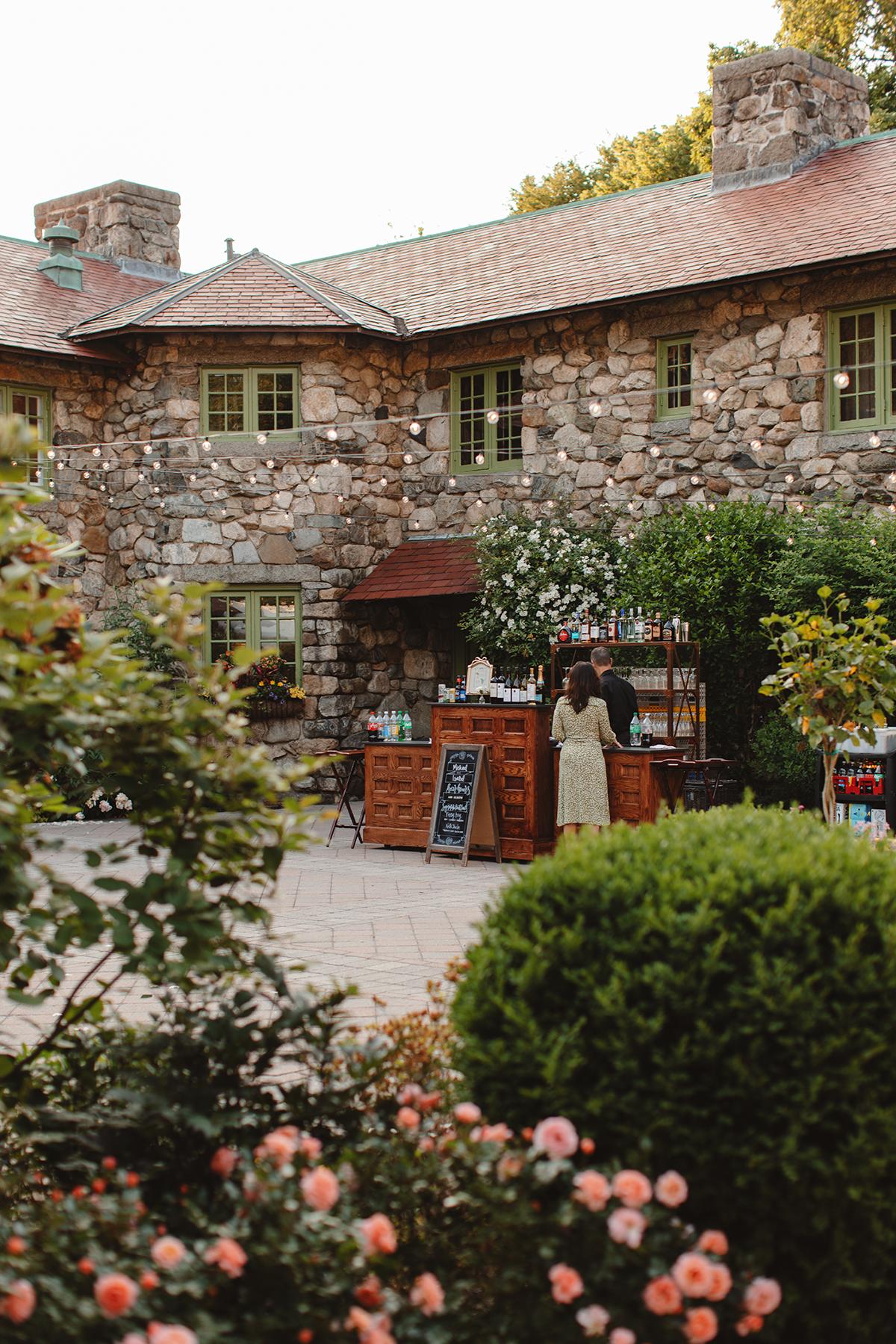 Historic stone building with ivy, flower garden, and a small outdoor market.