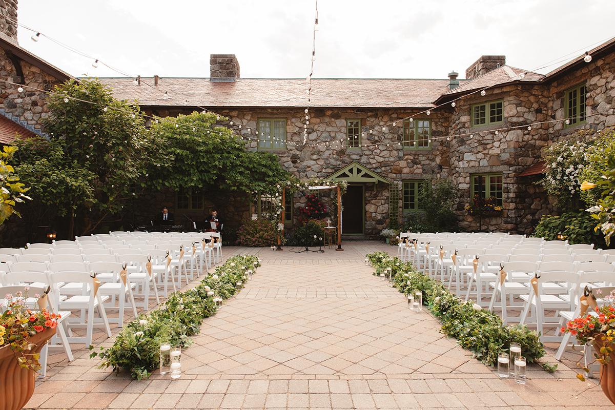Outdoor wedding setup with rows of white chairs facing a stone building.