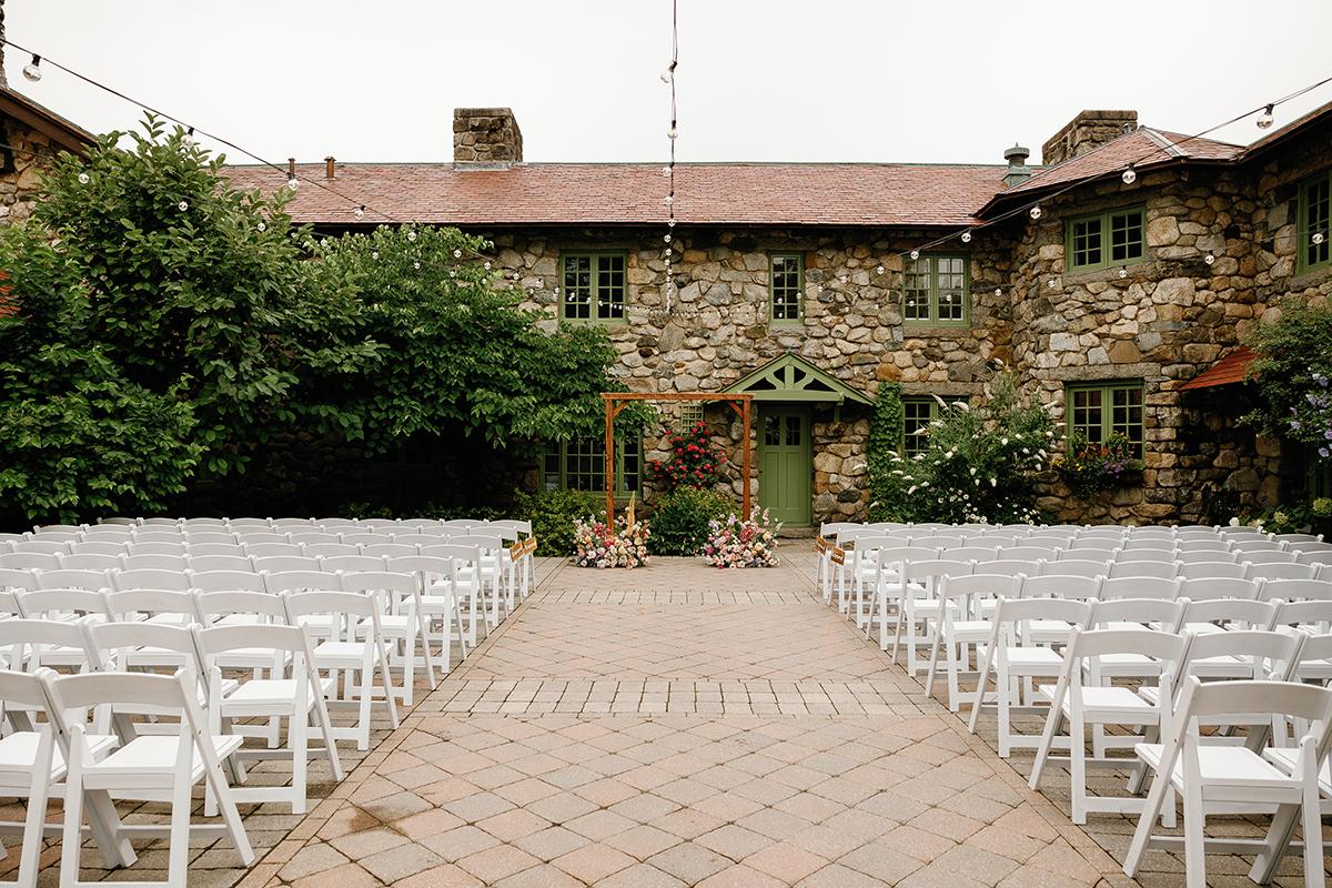 Courtyard set up for a wedding with white chairs and a floral arch.