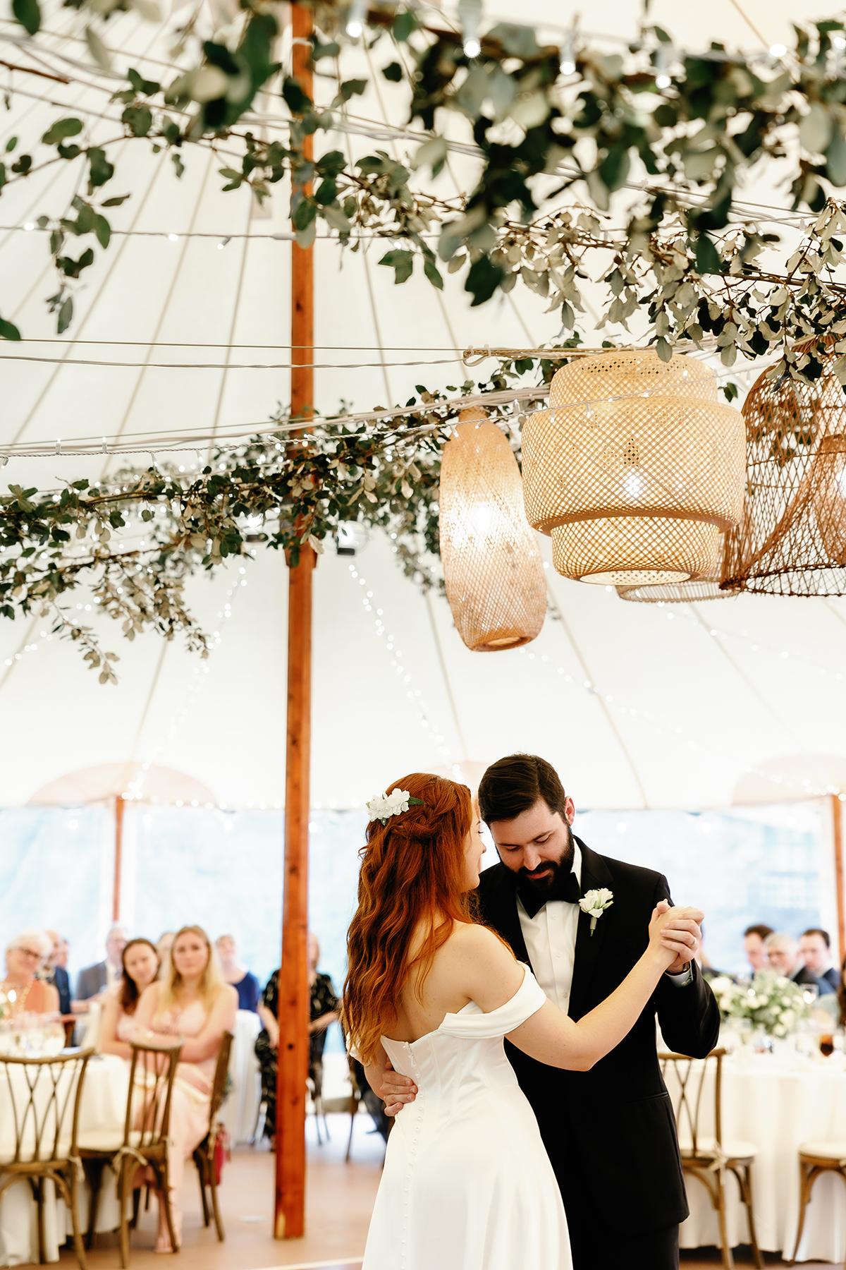 Bride and groom dancing under decorated tent.