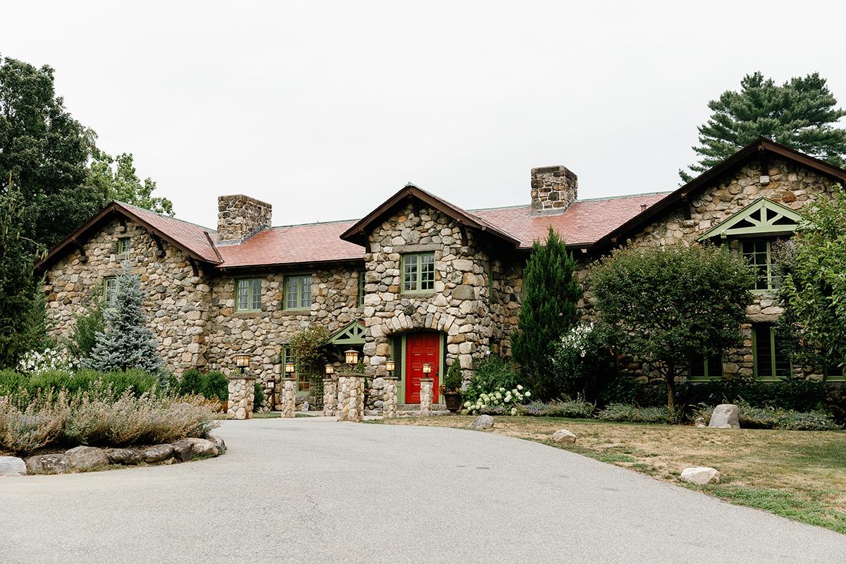 Stone house with red door, surrounded by greenery.
