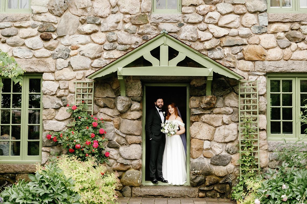 Bride and groom standing in a stone doorway, surrounded by greenery.