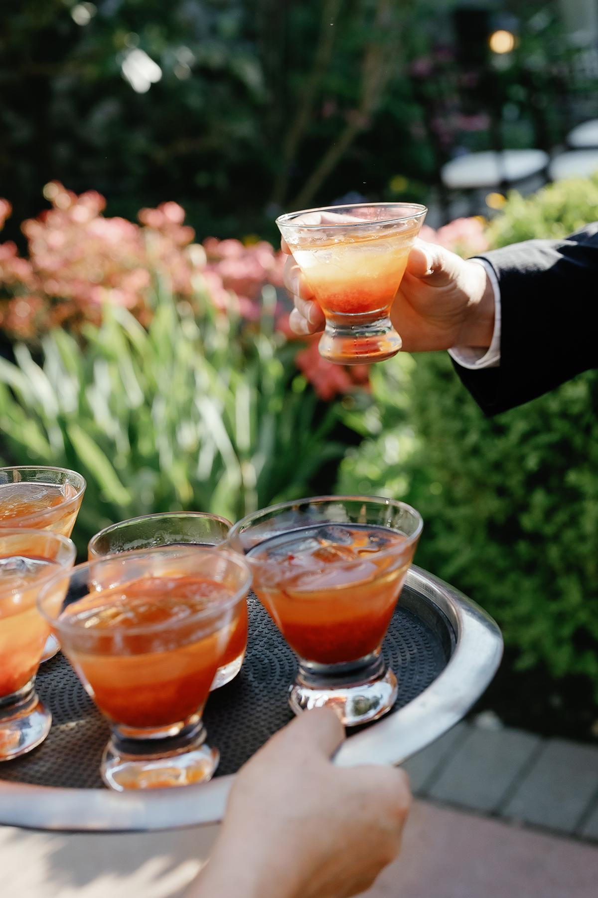 Cocktails on a tray in a garden setting, with one being served.