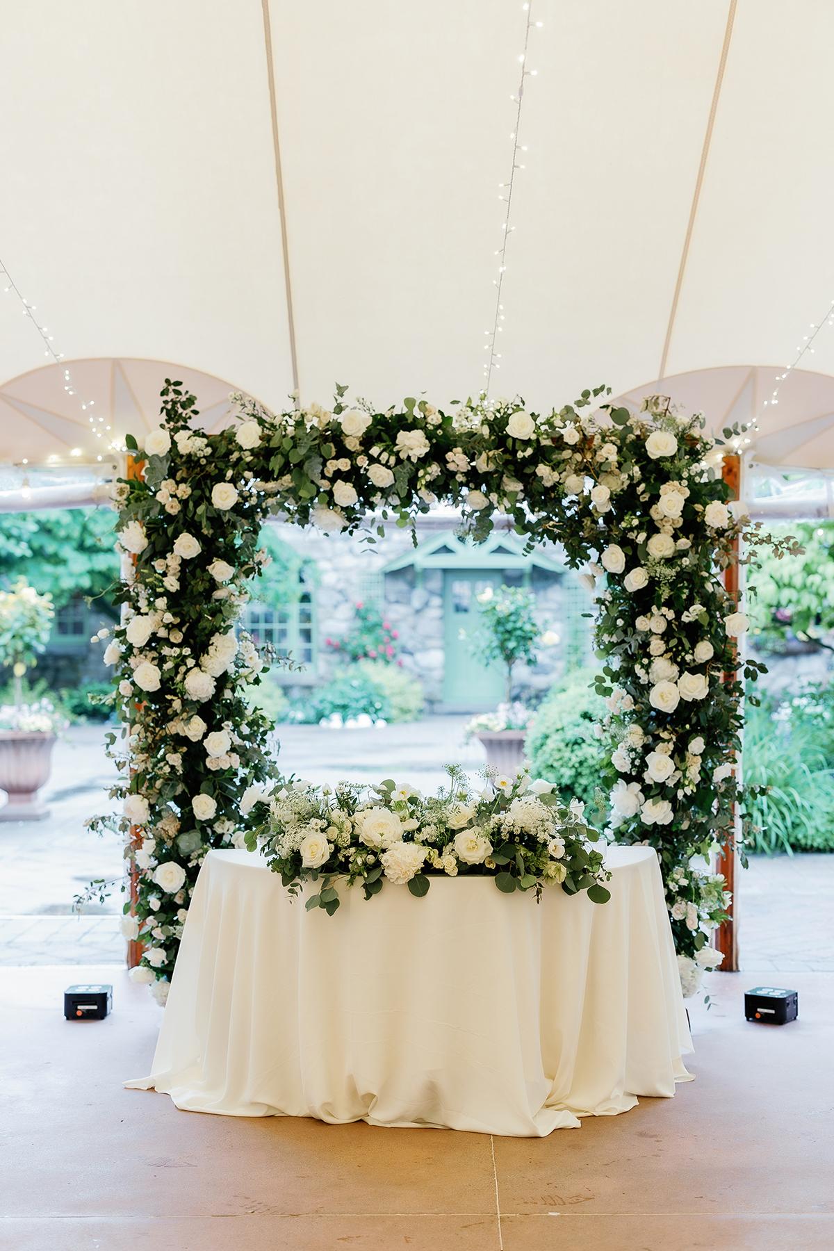 Floral arch over a round table in a garden setting.