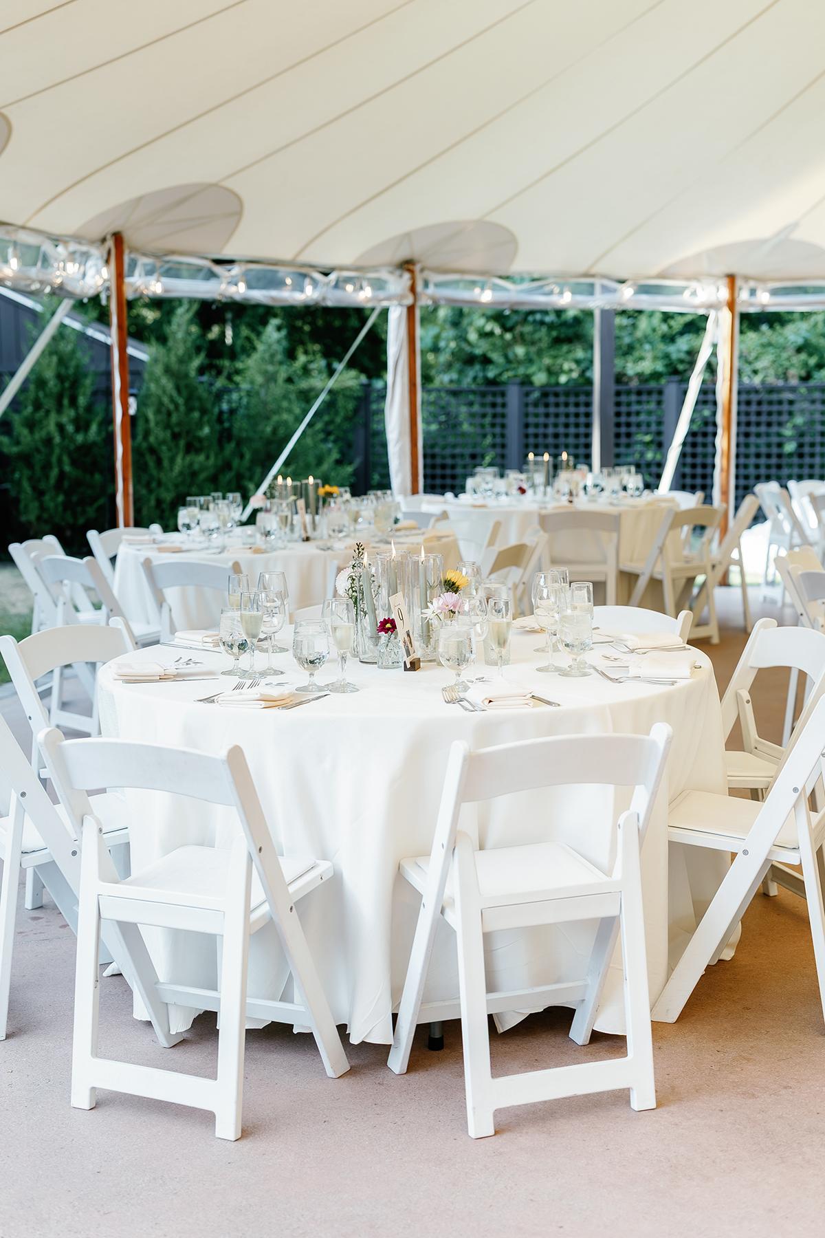 Elegant outdoor wedding setup with round tables and white chairs under a tent.