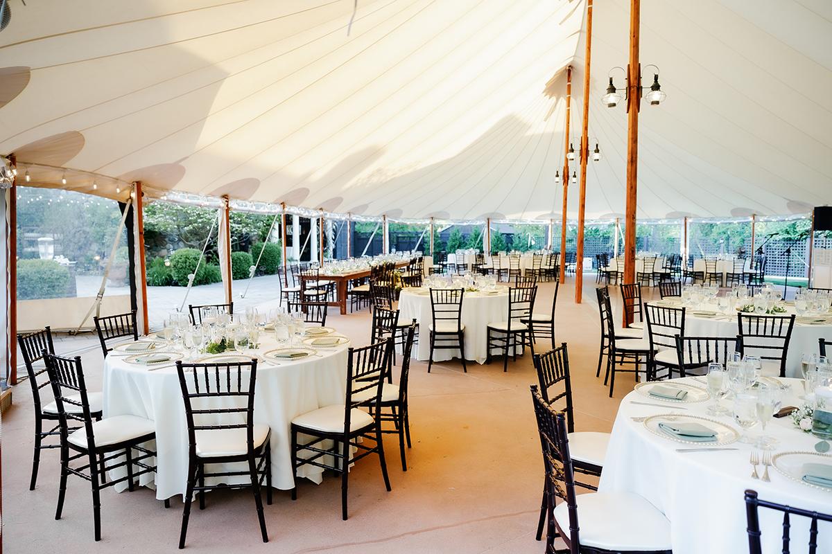 Elegant outdoor wedding tent with round tables set for dining.