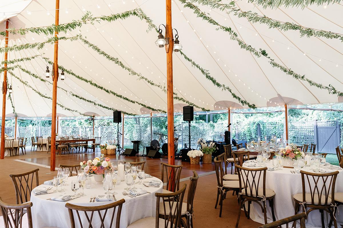 Wedding reception tent with decorated tables and hanging greenery.