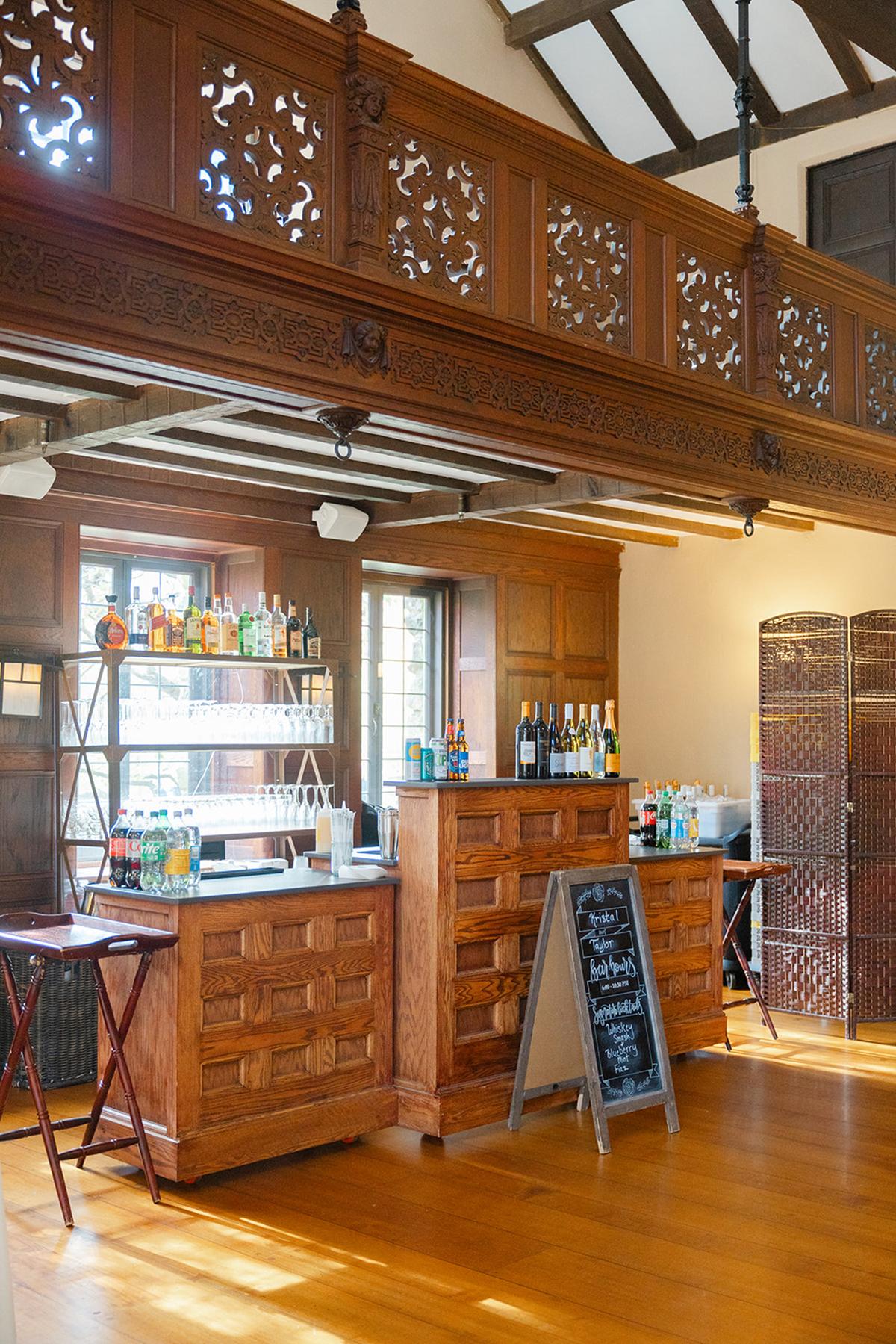 Cozy bar with wood paneling and shelves of bottles, lit by sunlight.