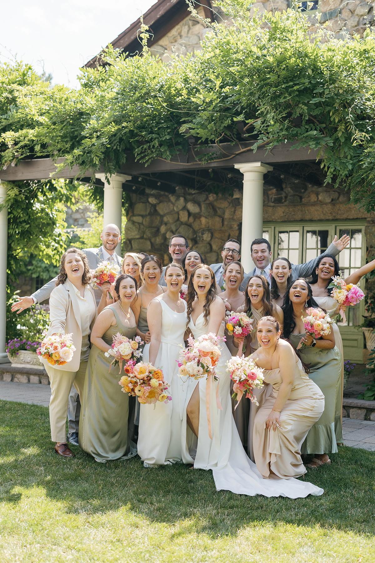 Wedding party posing cheerfully in garden, holding vibrant flower bouquets.