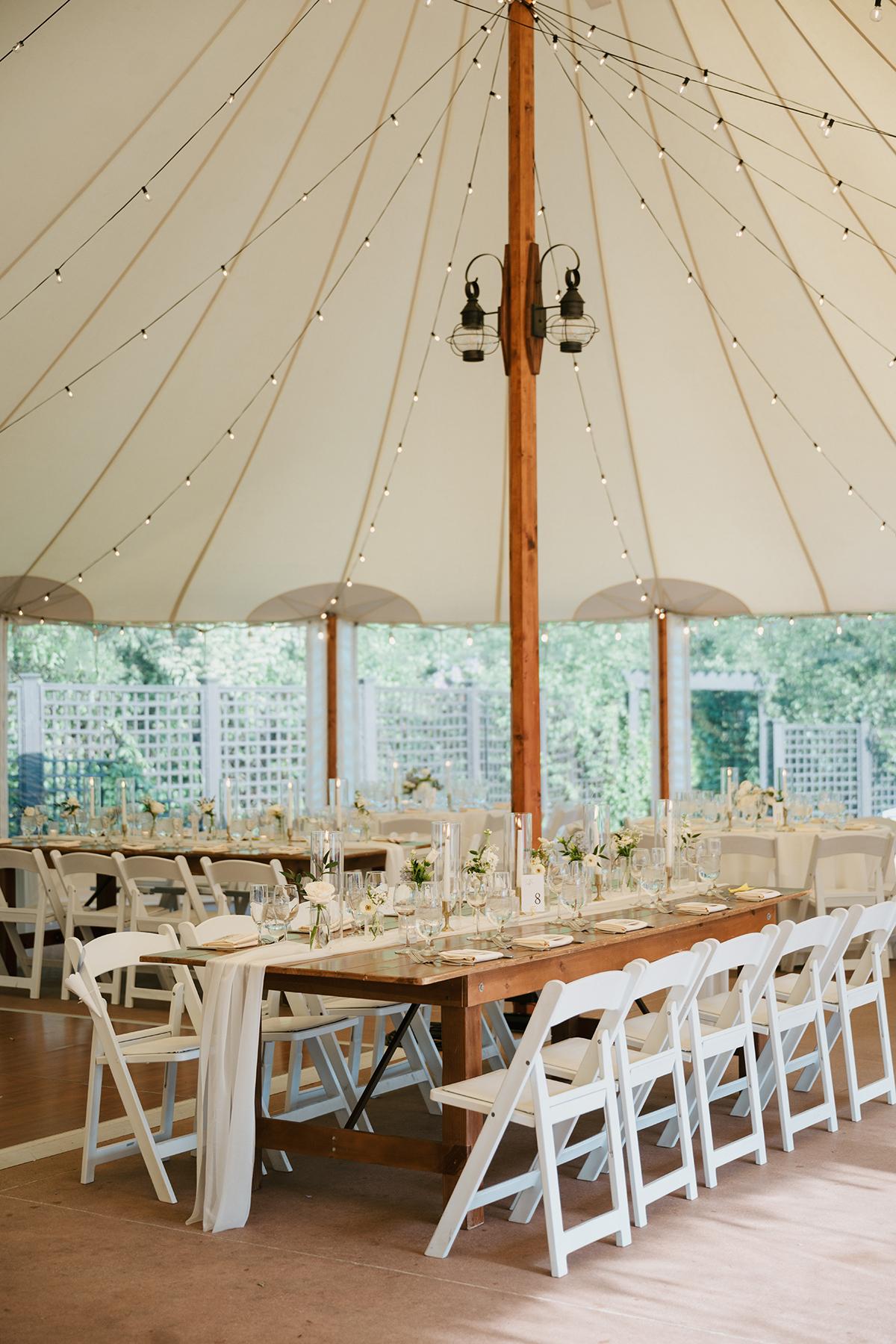 Wedding reception tent with wooden tables and white chairs.