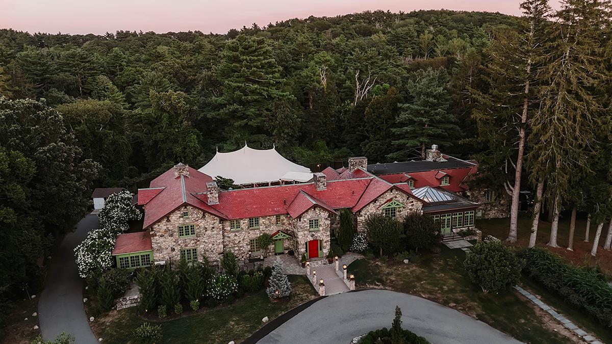 Large stone mansion with red roof, surrounded by trees at dusk.