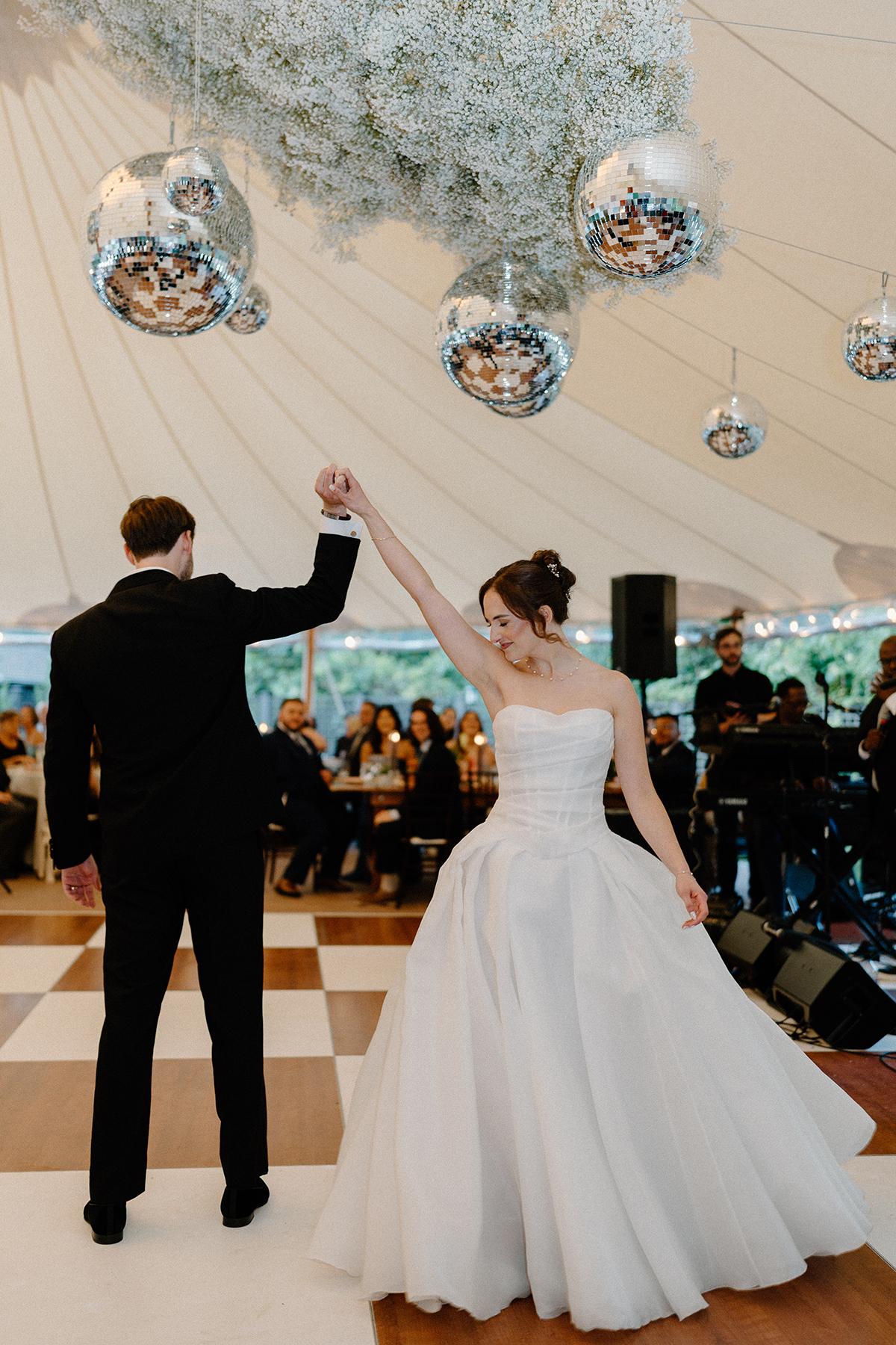 Bride and groom dancing under a tent with disco balls.