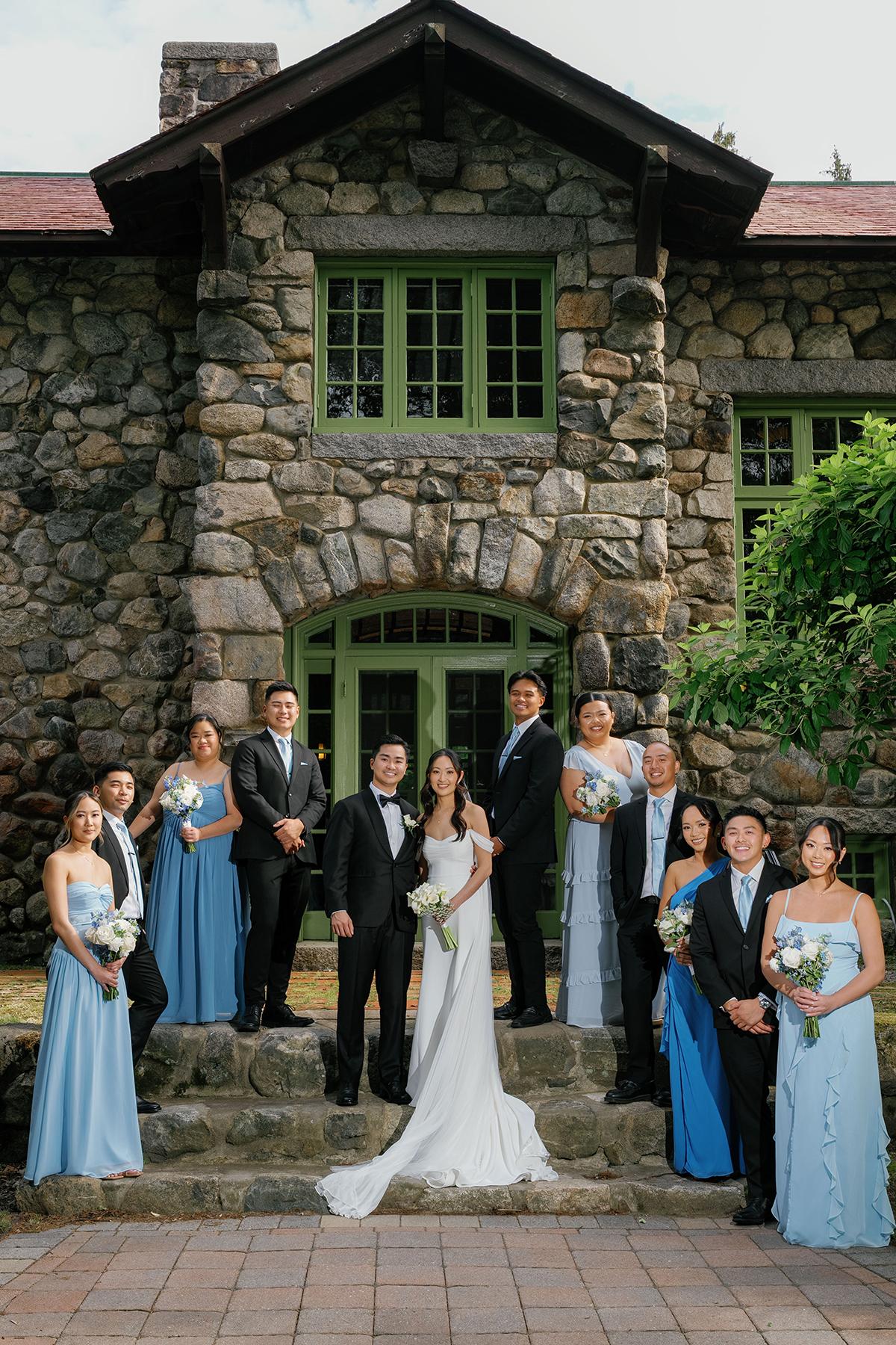 Wedding party poses in front of a stone building, bridesmaids in blue dresses.