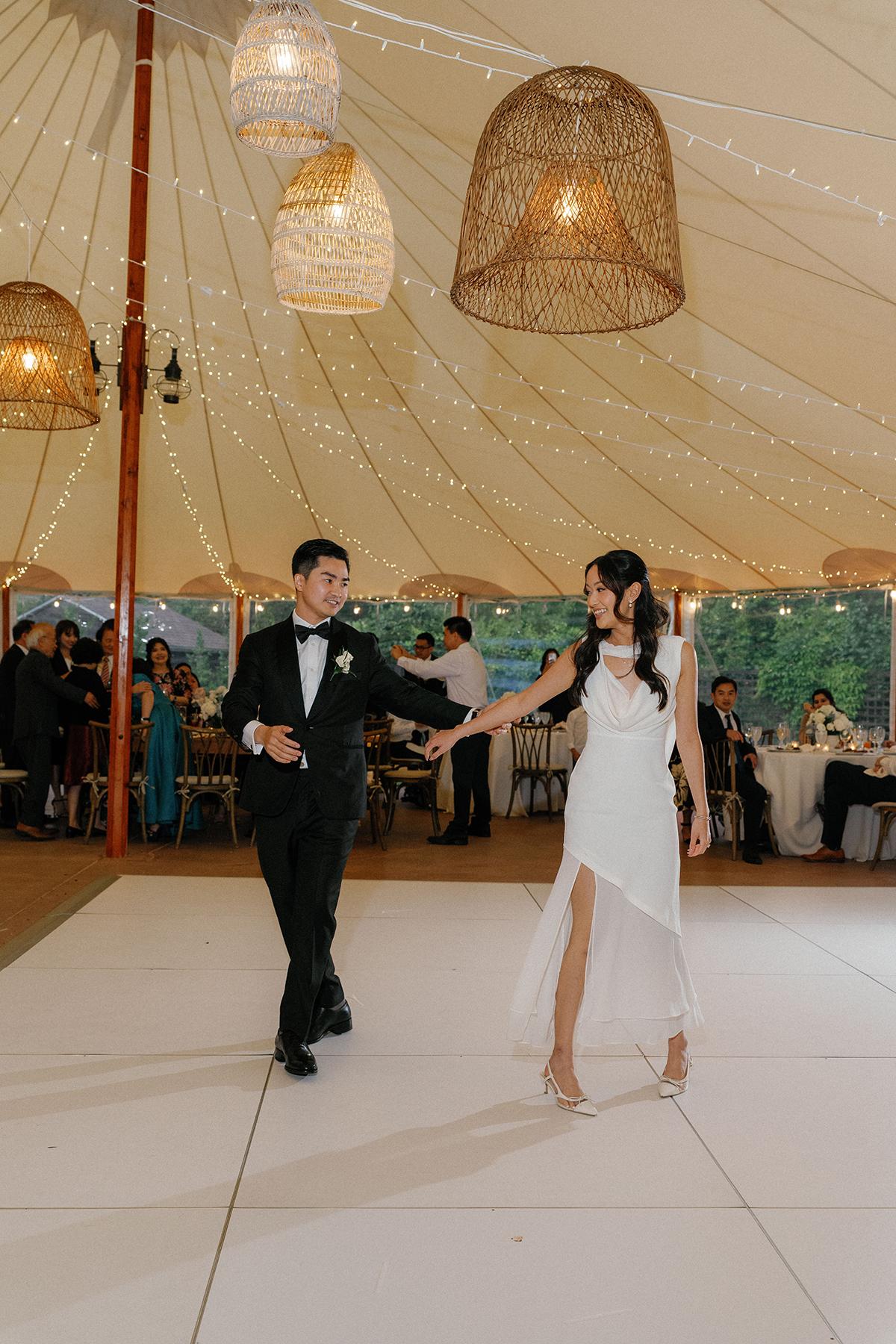 Couple dancing in a tent with warm lighting and guests seated in the background.