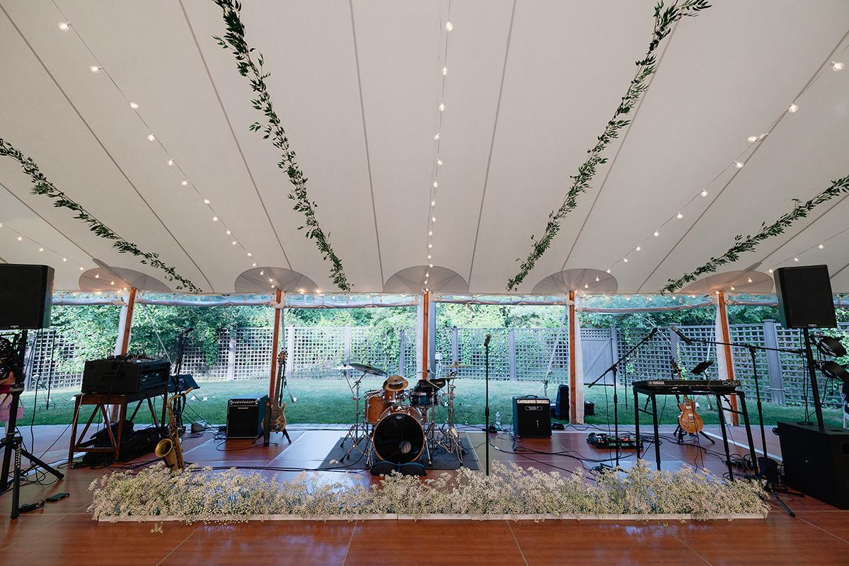 Outdoor wedding stage with instruments under a tent, greenery decorations.