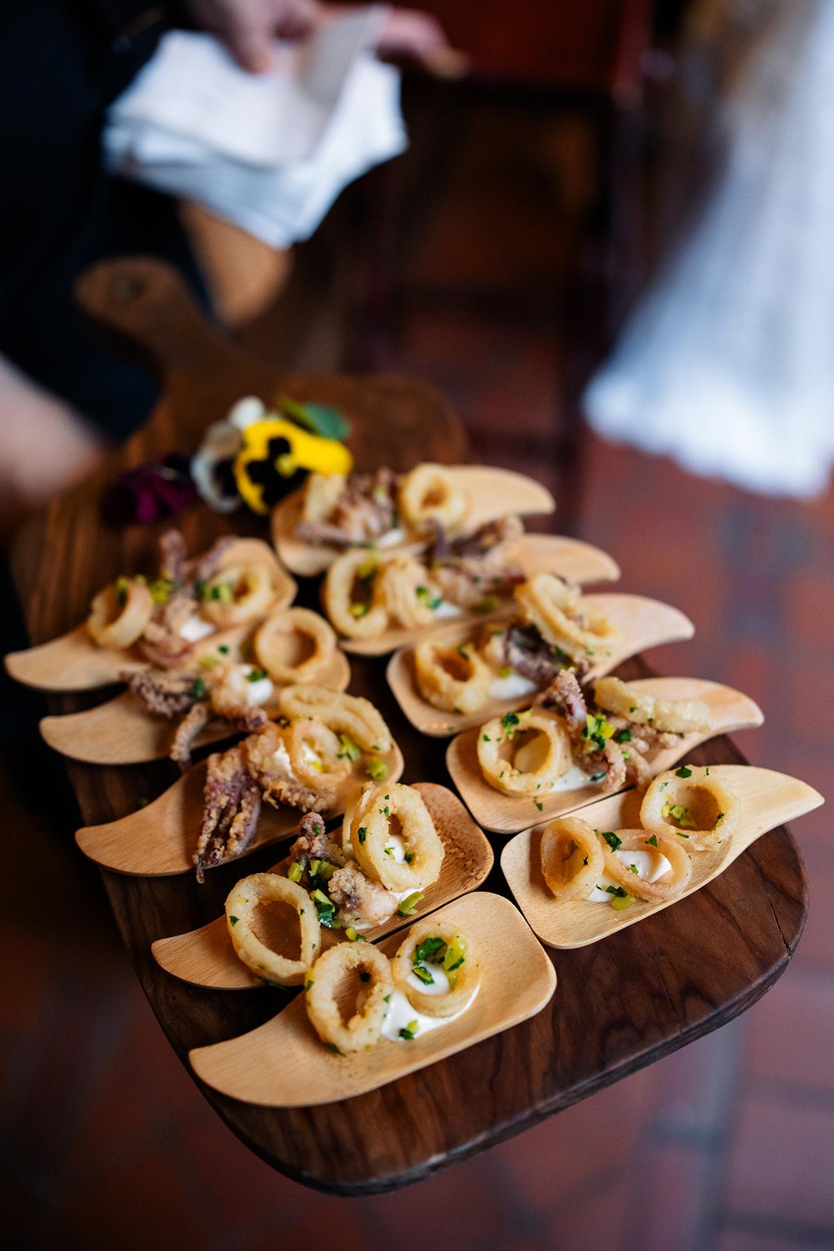 Appetizers on wooden spoons garnished with herbs and flowers.