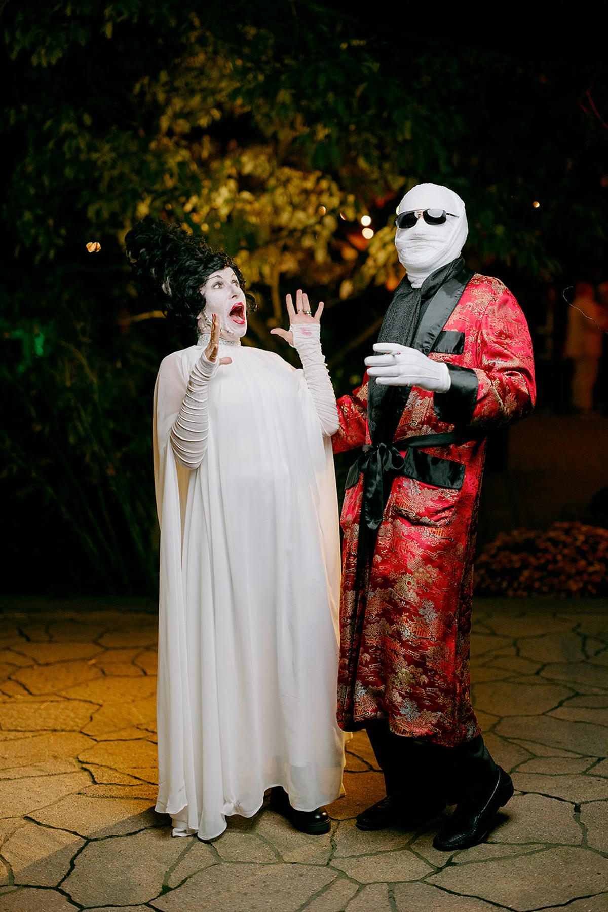 Two people in Halloween costumes pose under night lights.