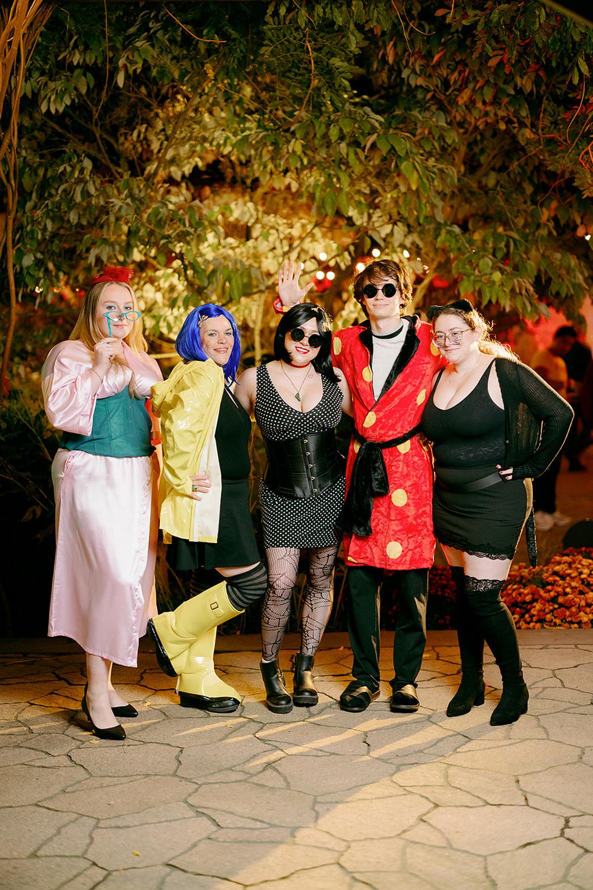 Five people in colorful costumes pose together outdoors at night.