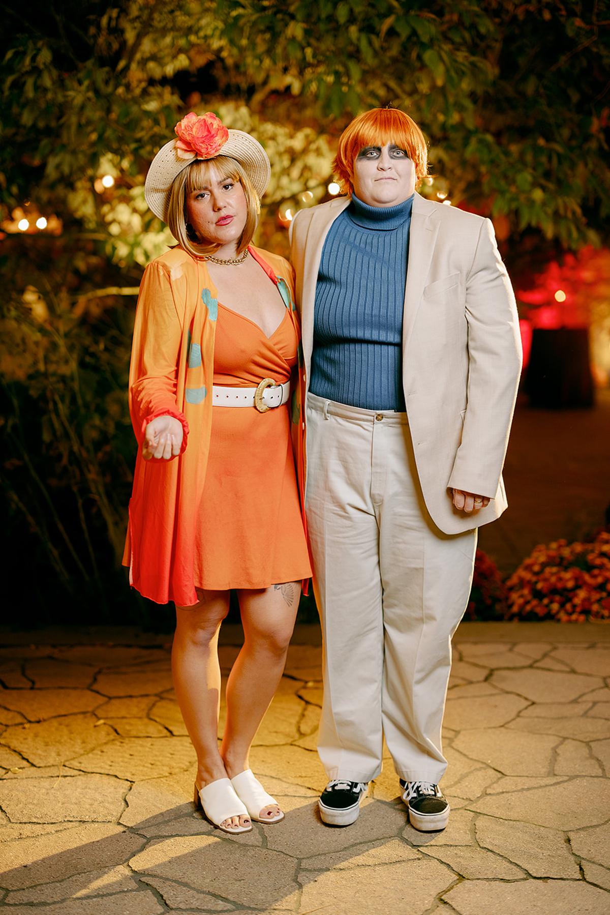 Two people in colorful, retro outfits standing together outdoors at night.