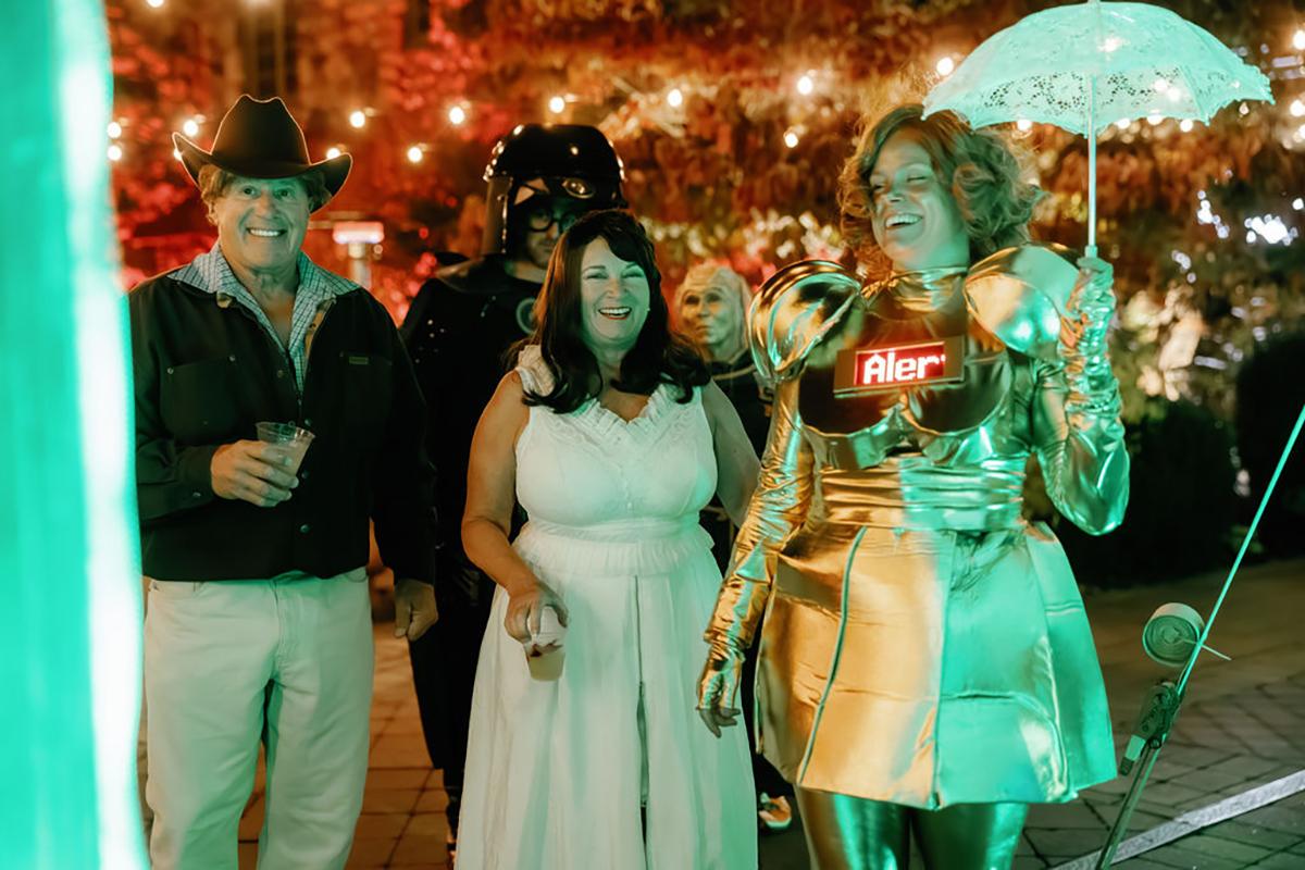 Group in costumes, one in gold armor, standing under string lights at night.