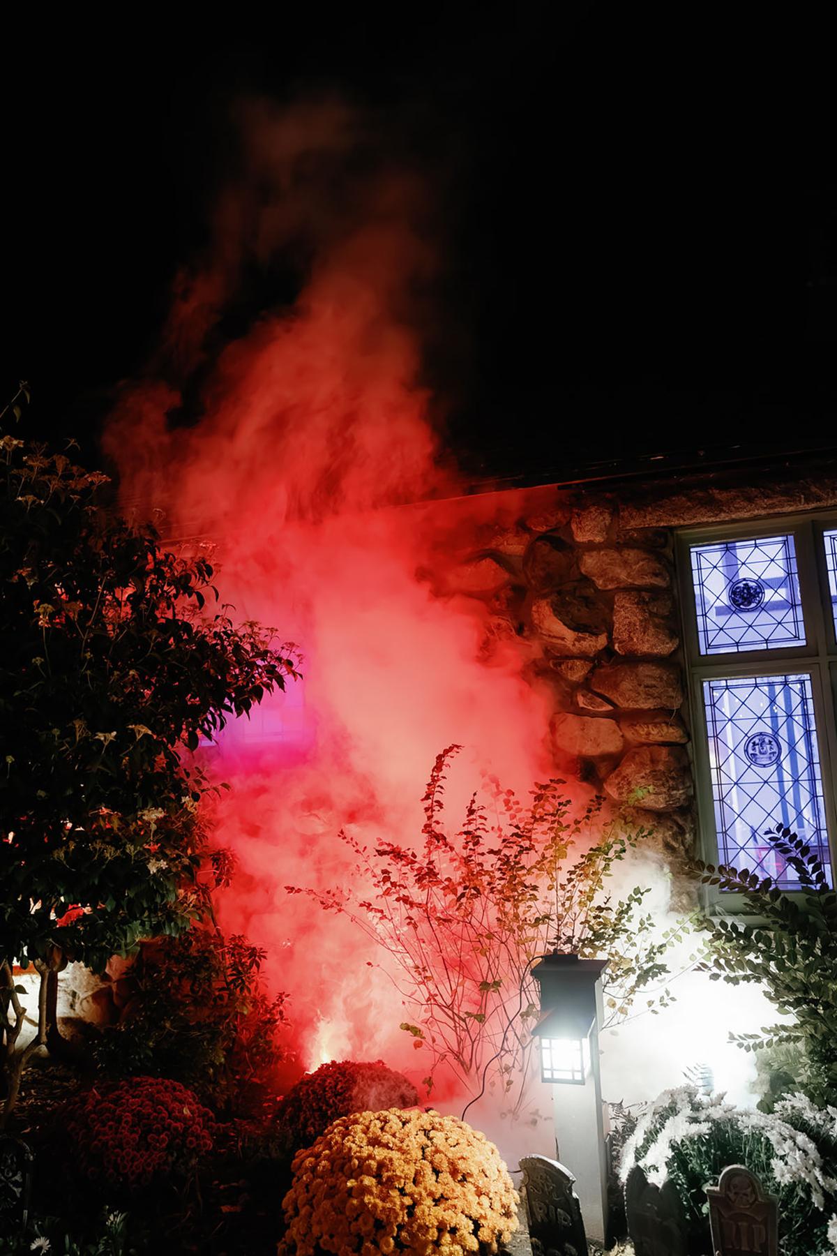 Red smoke billowing near a stone building at night, illuminated by colorful lights.