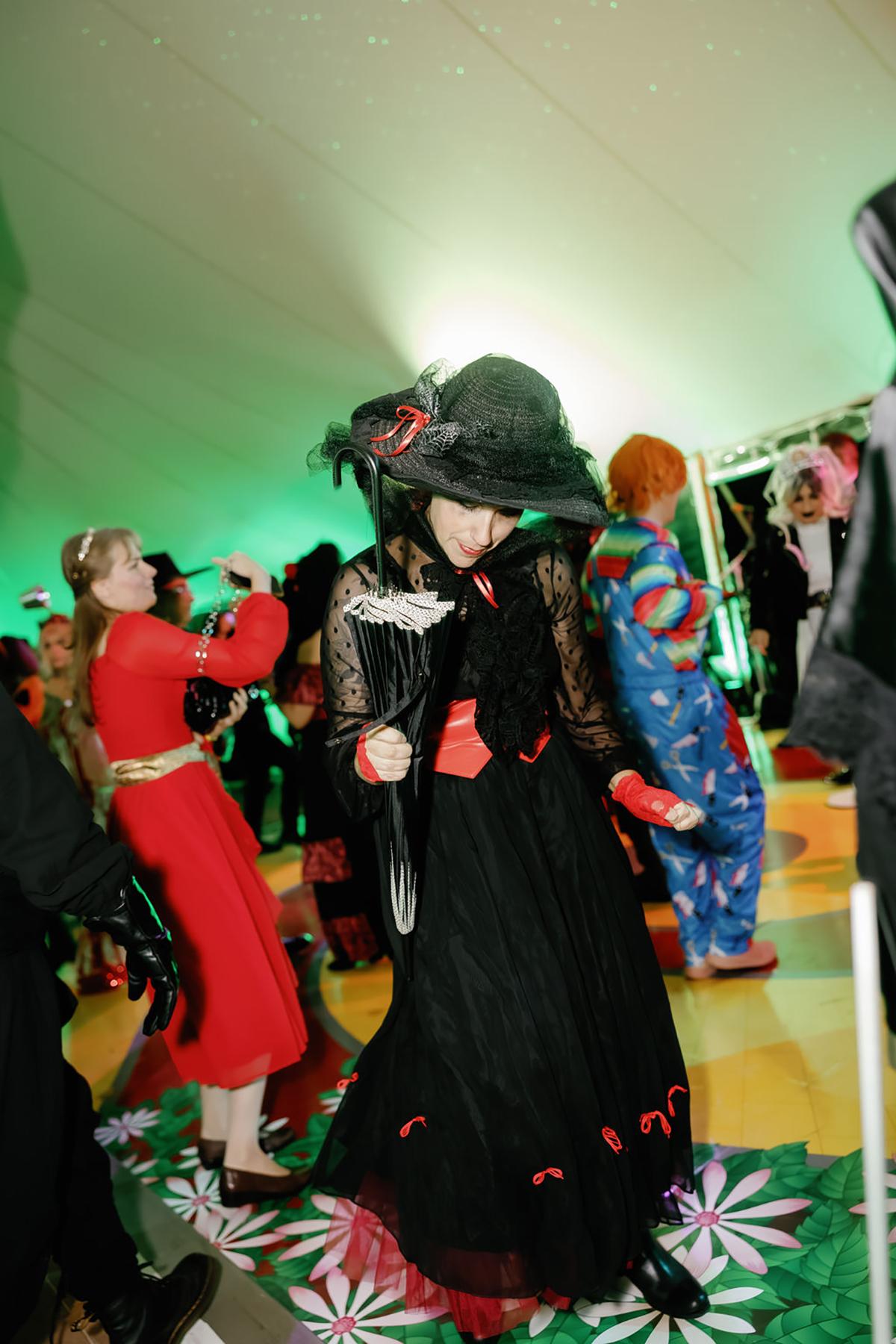 Dancing in costume at a lively party, wearing a black hat and dress.
