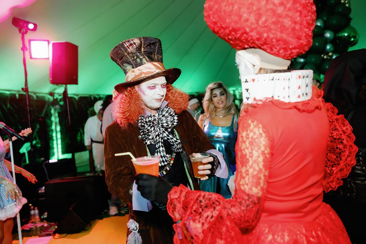 Costumed people at a party with colorful lighting and drinks in hand.