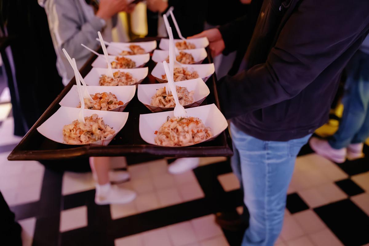 Tray of appetizers with forks at an event on checkered floor.